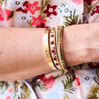 Close-up of a wrist wearing gold bracelets with gemstones against a floral background
