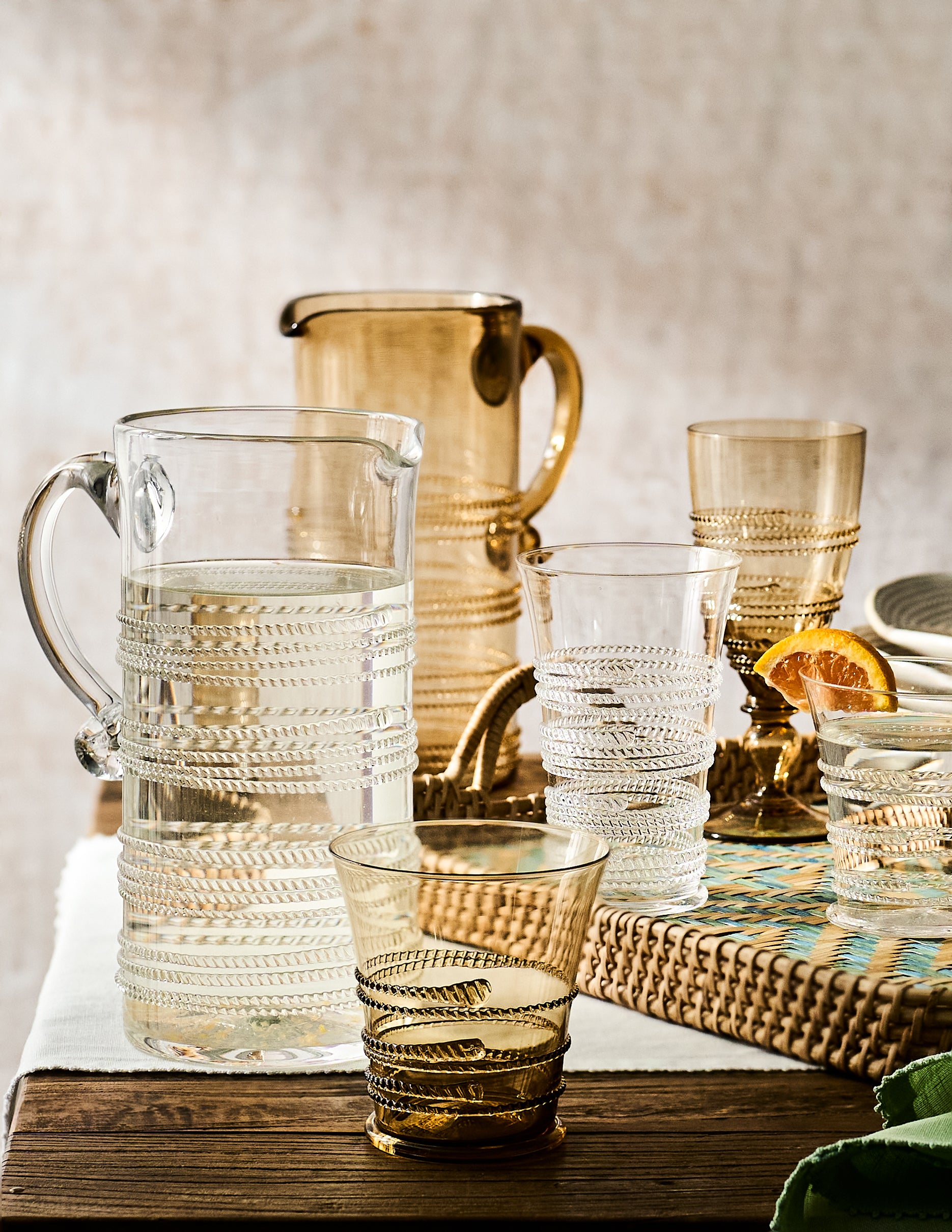 Set of glass pitchers and tumblers on a wooden surface with a neutral background